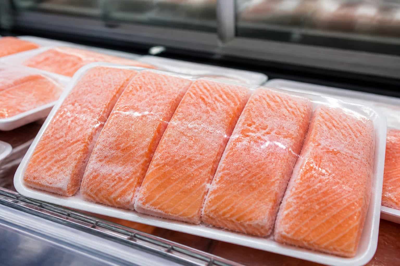 Frozen salmon portions on a white tray inside a supermarket freezer.