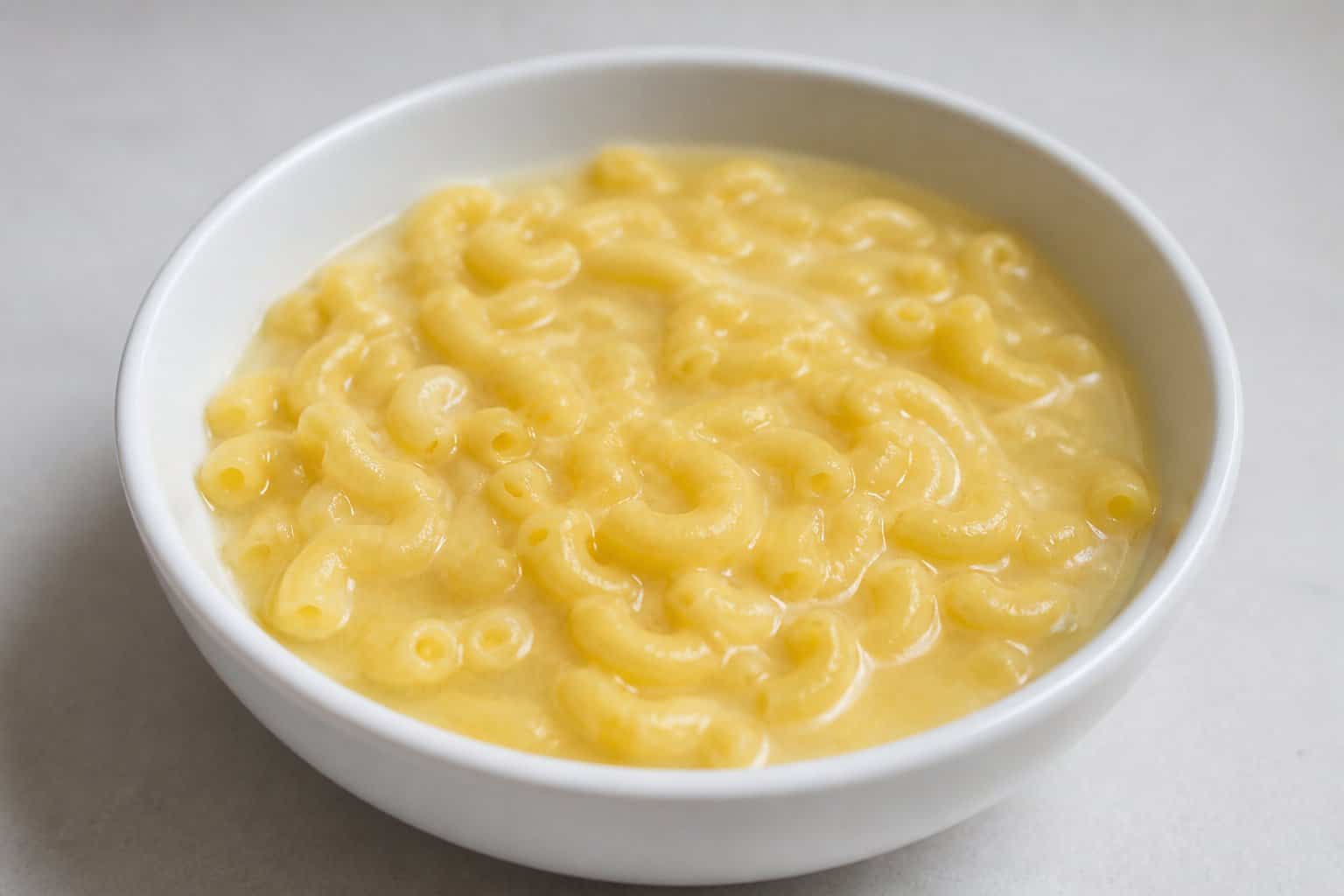 A bowl of bland, watery macaroni and cheese on a neutral surface.