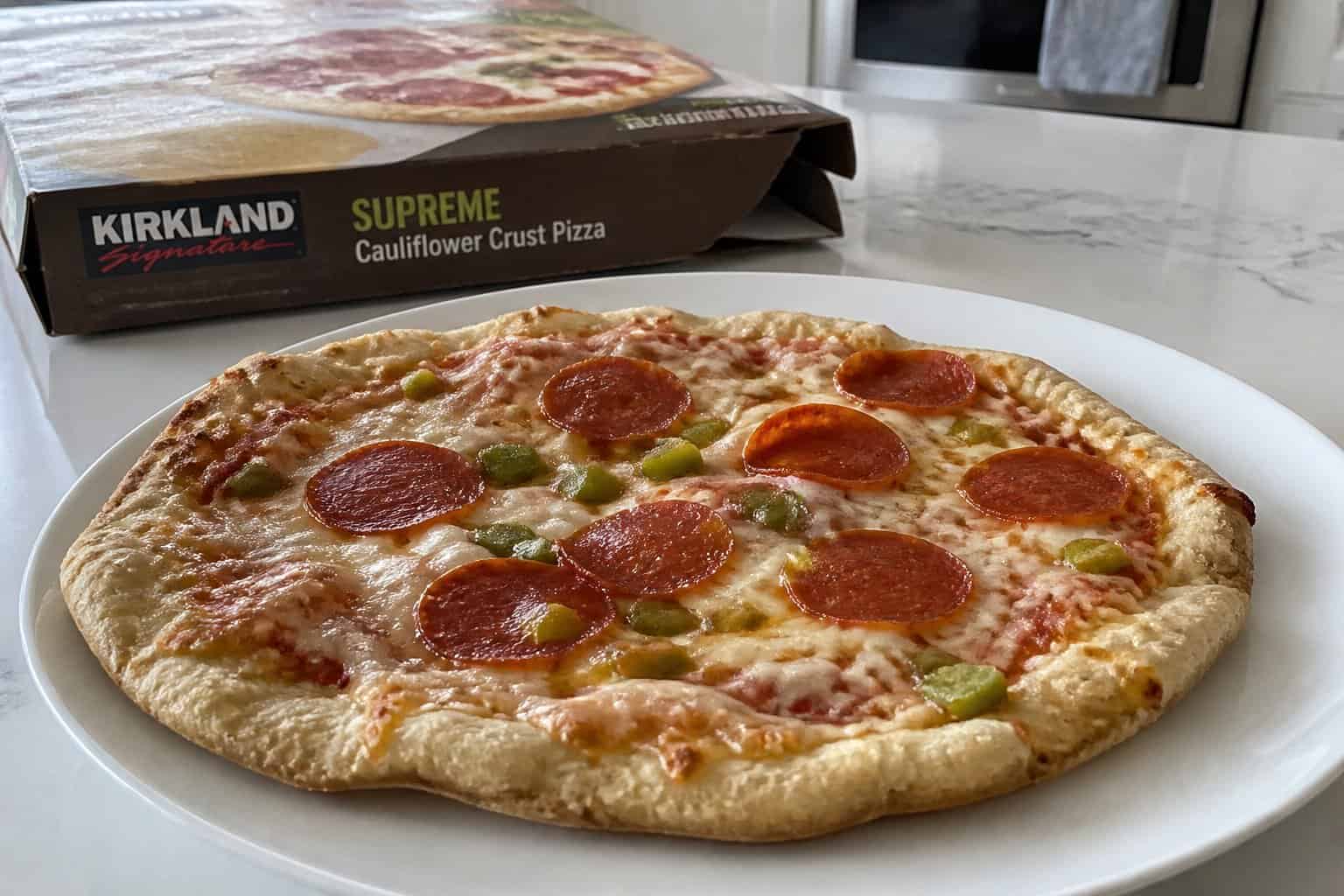 A frozen pizza with a soggy crust on a white plate on a kitchen countertop, with a Costco pizza box in the background.