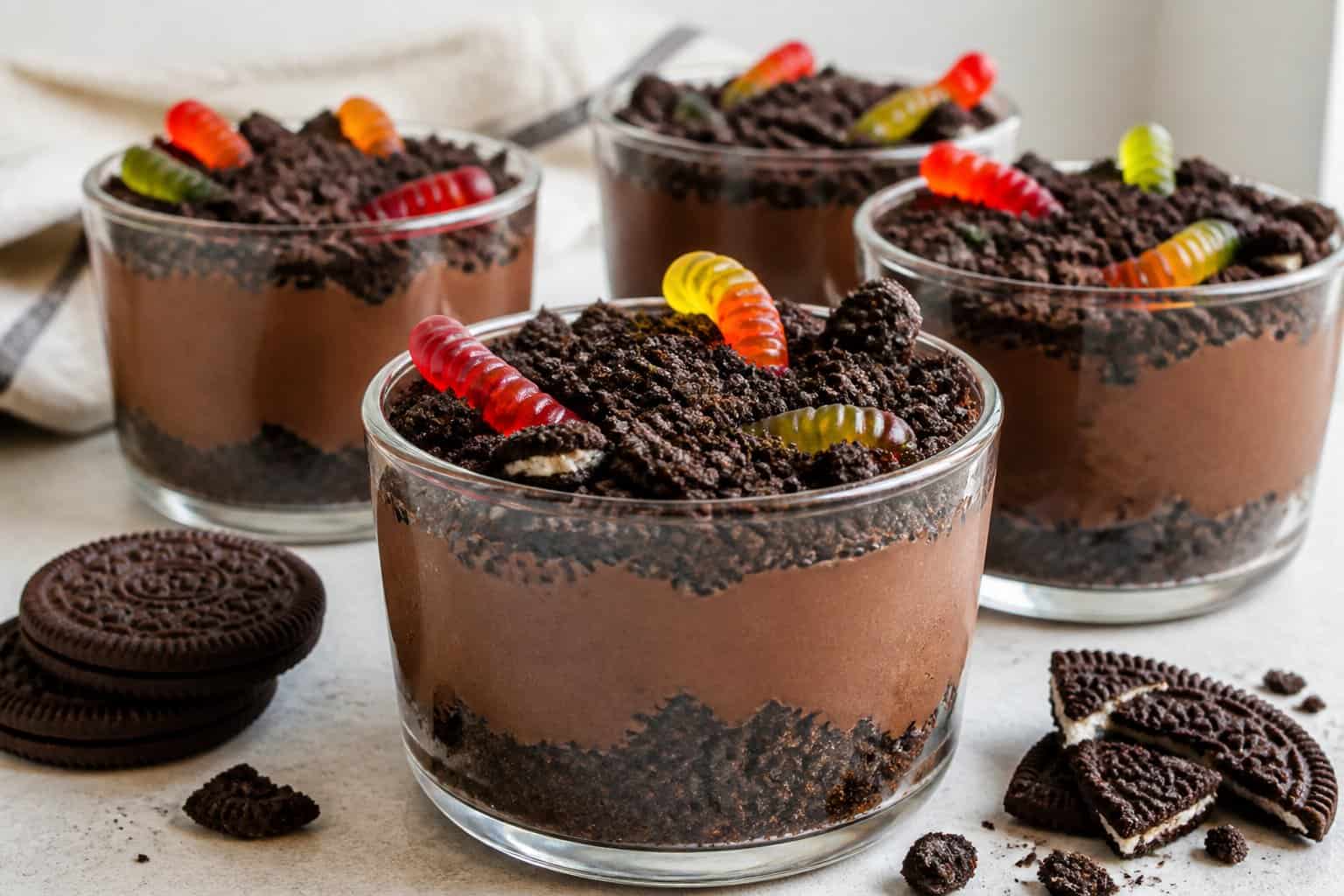Clear cups of chocolate pudding topped with crushed cookies and gummy worms.