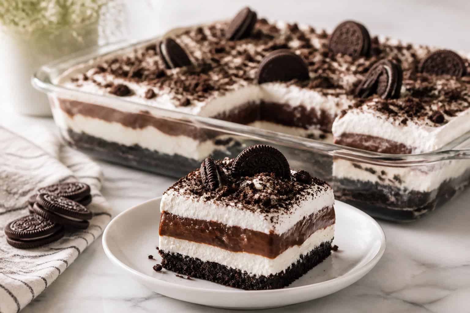 A layered chocolate and cream Oreo dessert topped with cookie crumbs and served with one slice cut out.