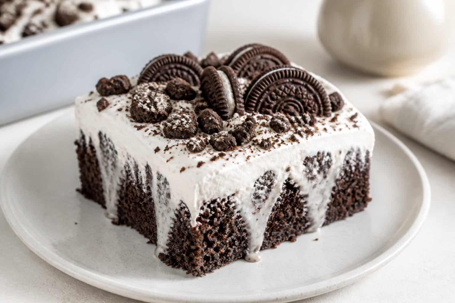 A slice of chocolate Oreo poke cake topped with white cream and crushed cookies.