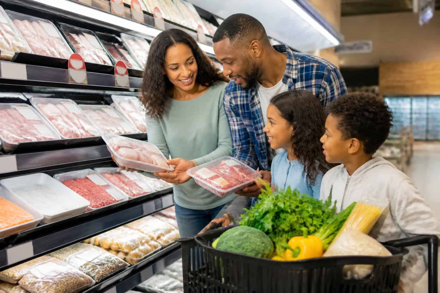 A shopper compares discounted protein options in a grocery store while planning meals with other fresh ingredients.