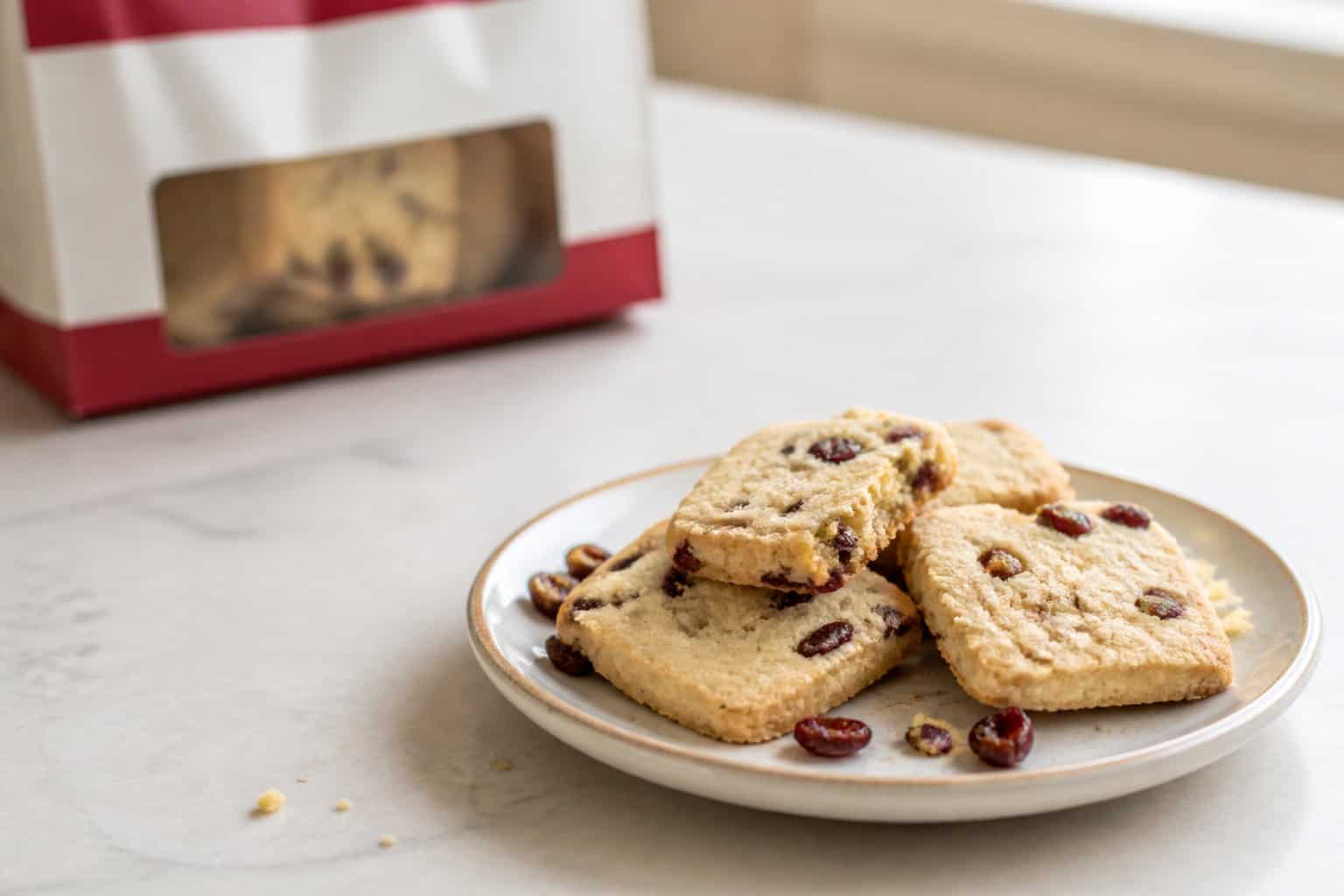 A plate of dry-looking cranberry butter cookies beside a blurred cookie package on a kitchen counter.