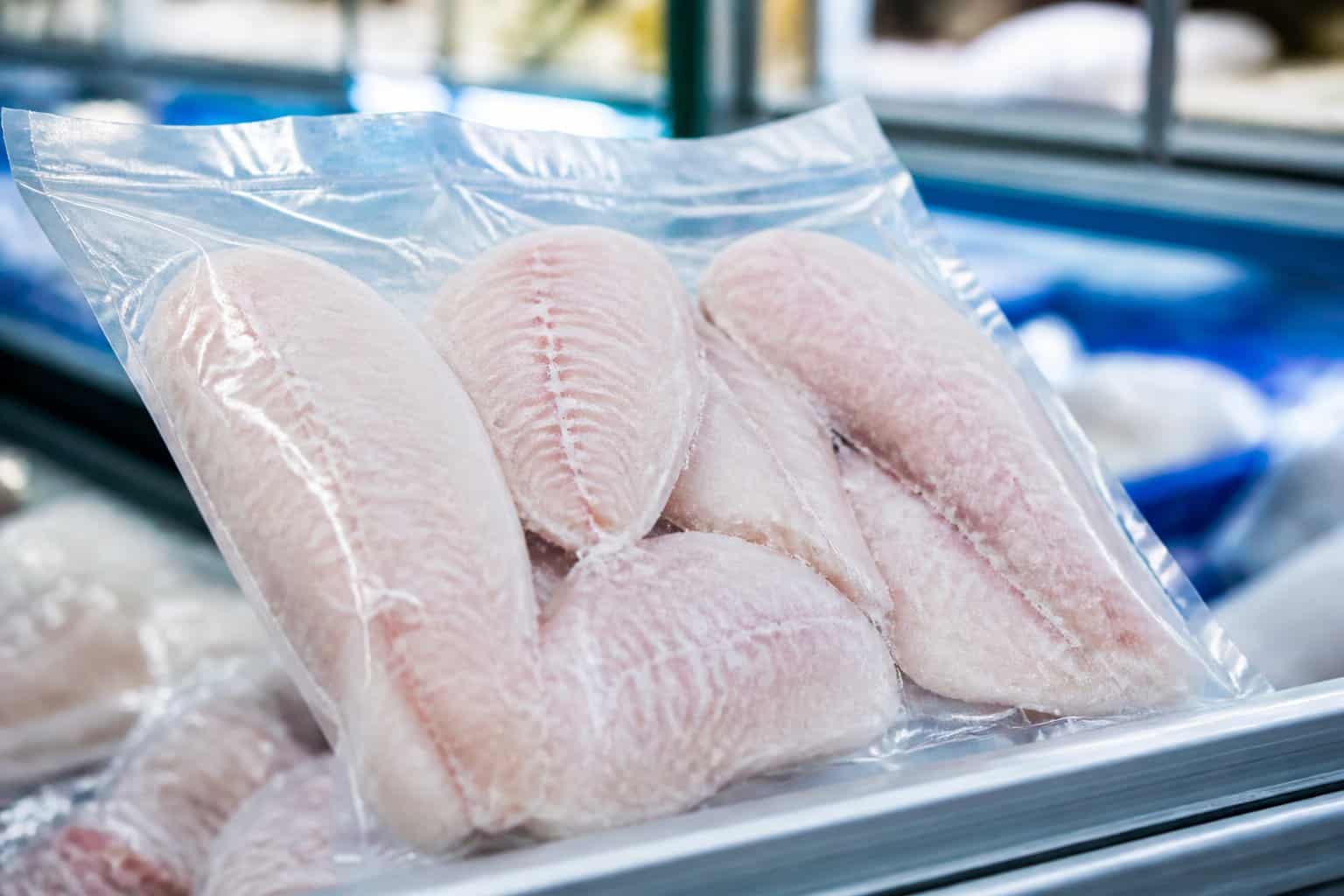 A sealed package of frozen tilapia fillets displayed in a refrigerated grocery case.