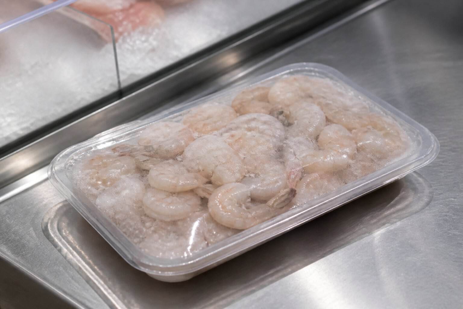 A packaged tray of small shrimp on a chilled seafood counter.
