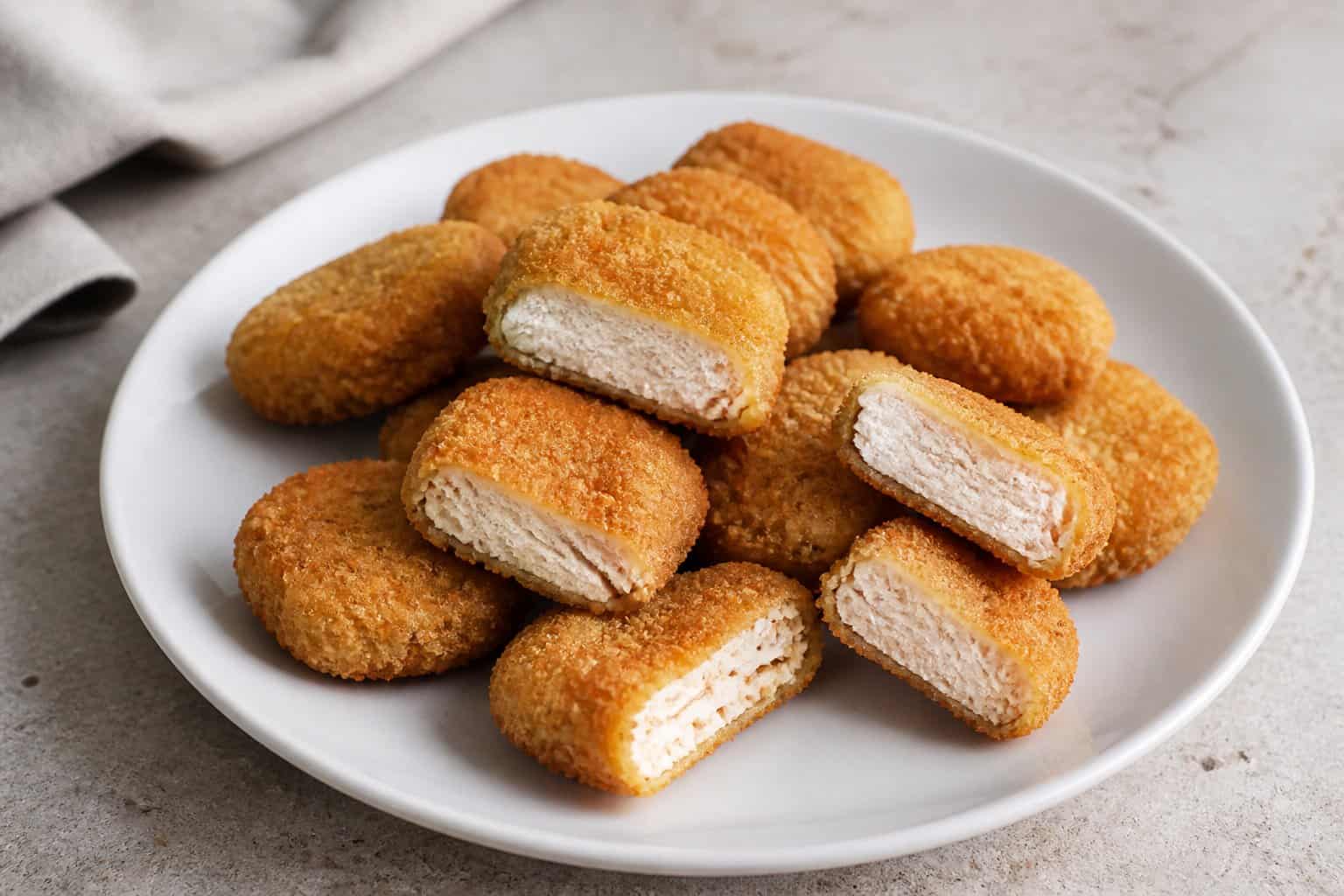 A plate of golden-brown chicken nuggets, with several pieces showing their pale interior.