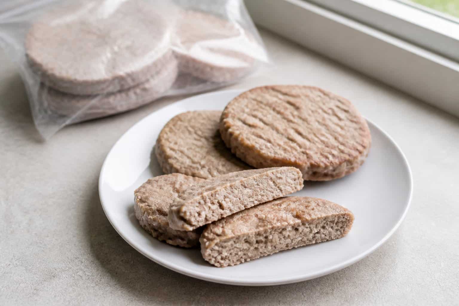Several plain turkey burger patties sit on a white plate, with one cut open to show its dense interior.