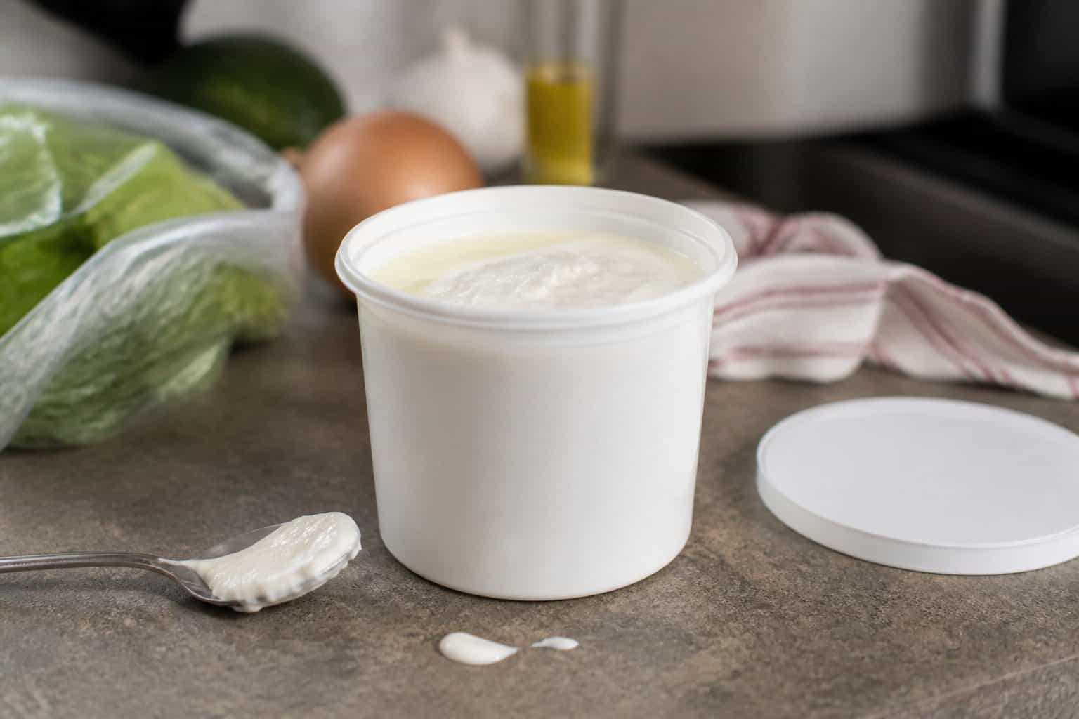 A plain tub of sour cream sits on a kitchen counter beside a spoonful of sour cream.