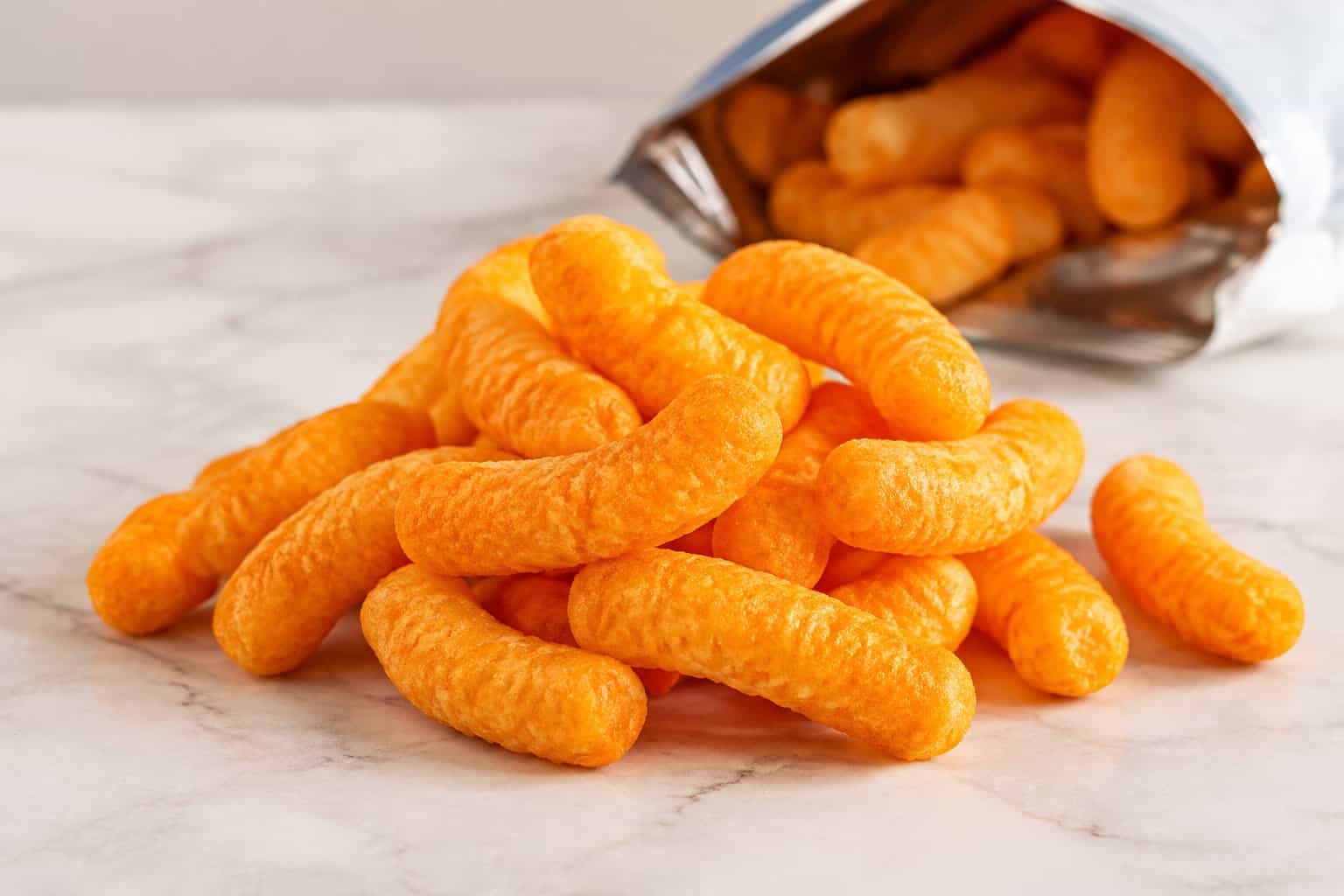 Orange cheese puffs beside a snack bag.