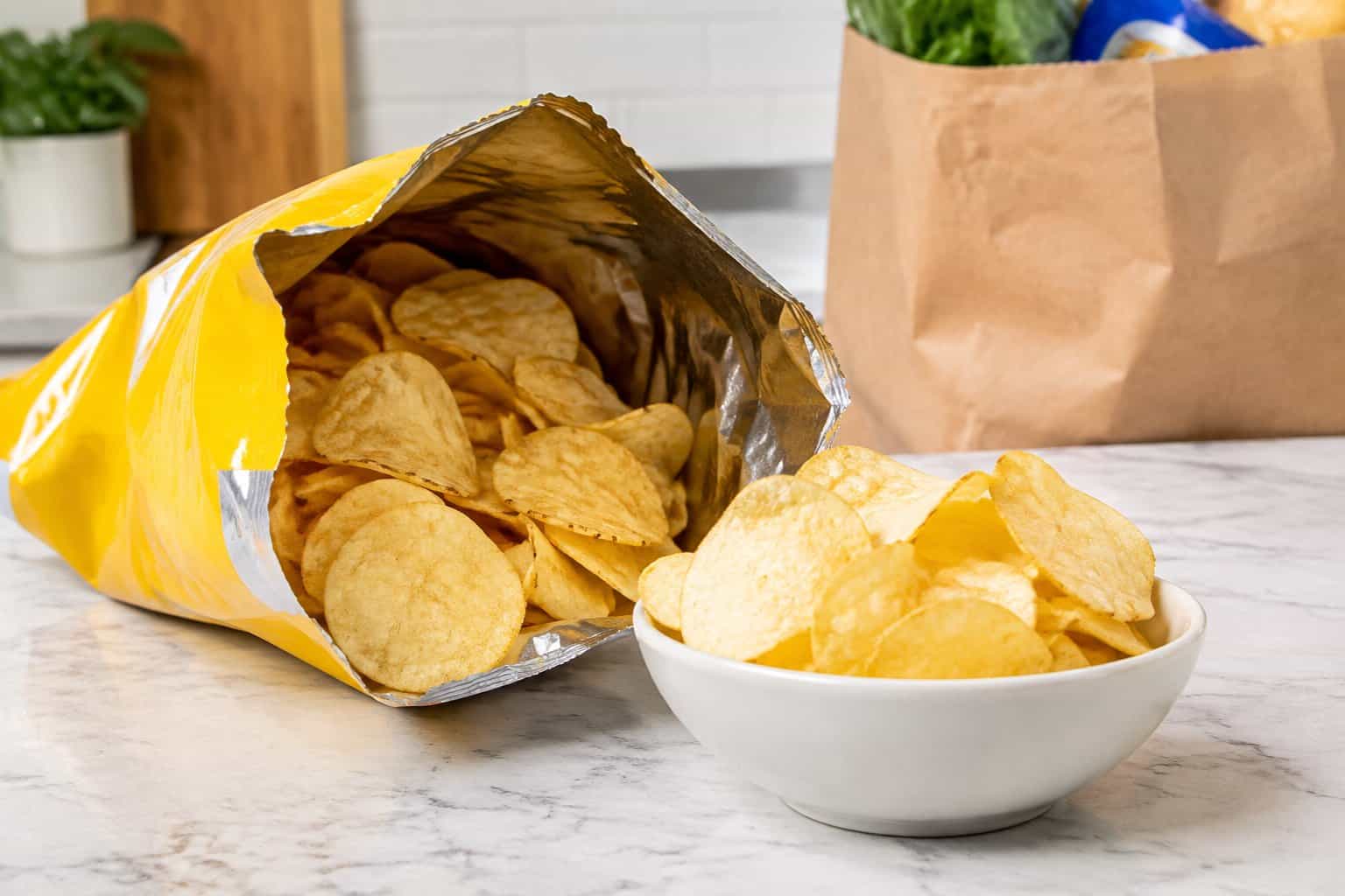 A bag of potato chips beside a small serving of chips on a kitchen counter.