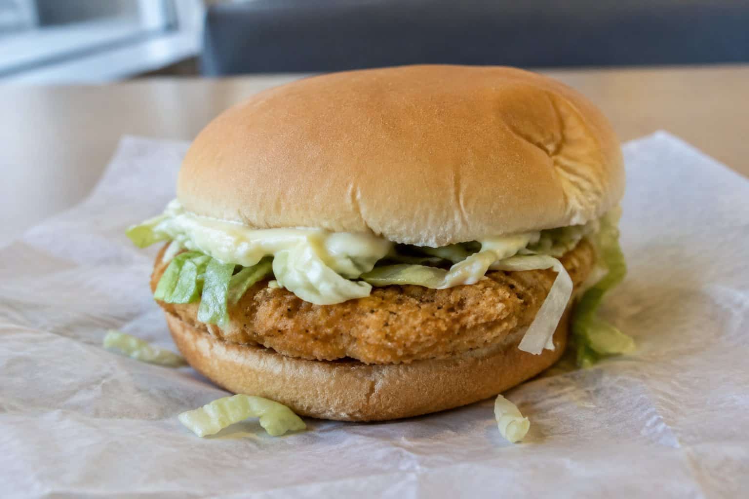 A chicken sandwich with shredded lettuce and mayonnaise on a paper wrapper.
