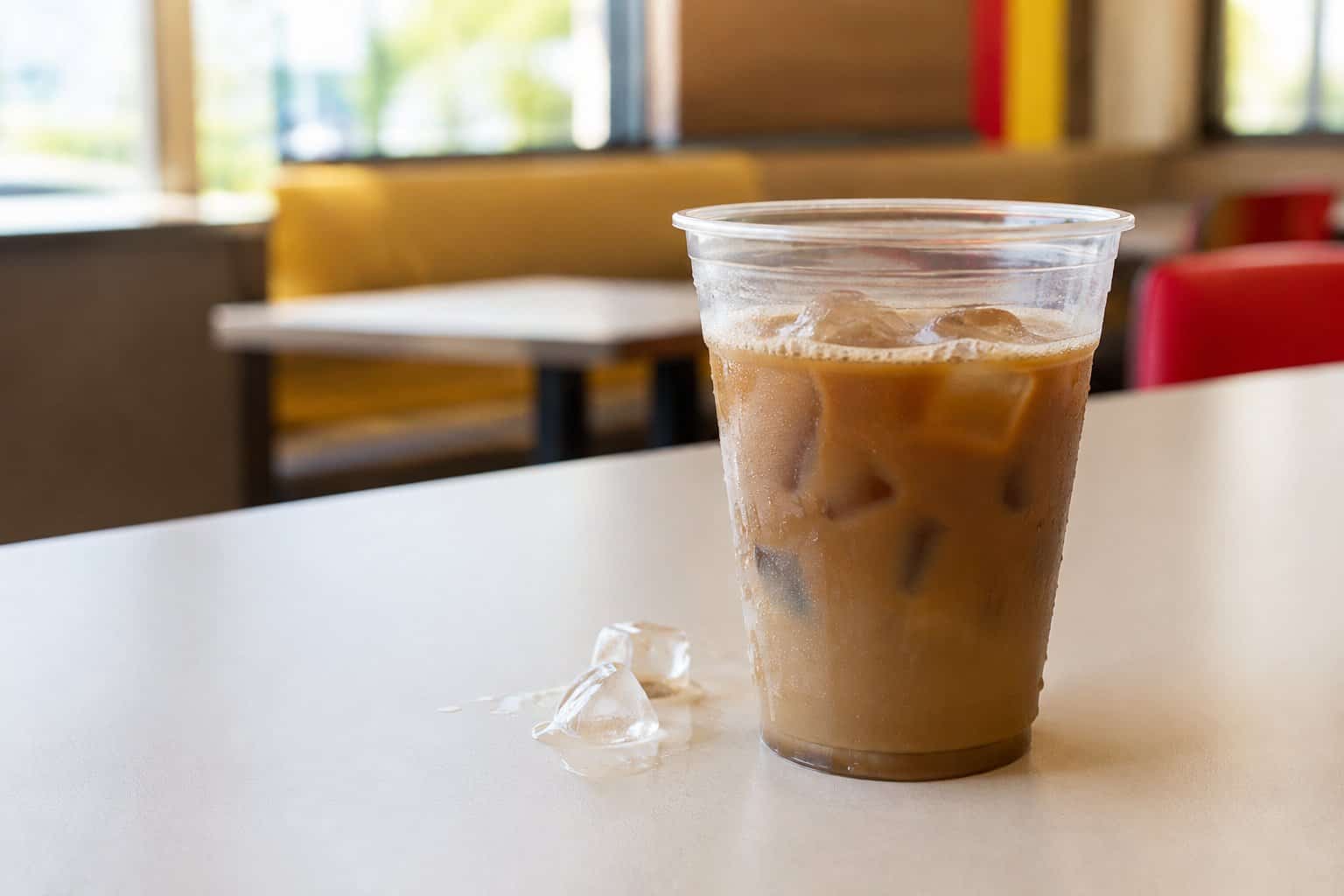 A cup of iced coffee sits on a table in a fast-food restaurant.