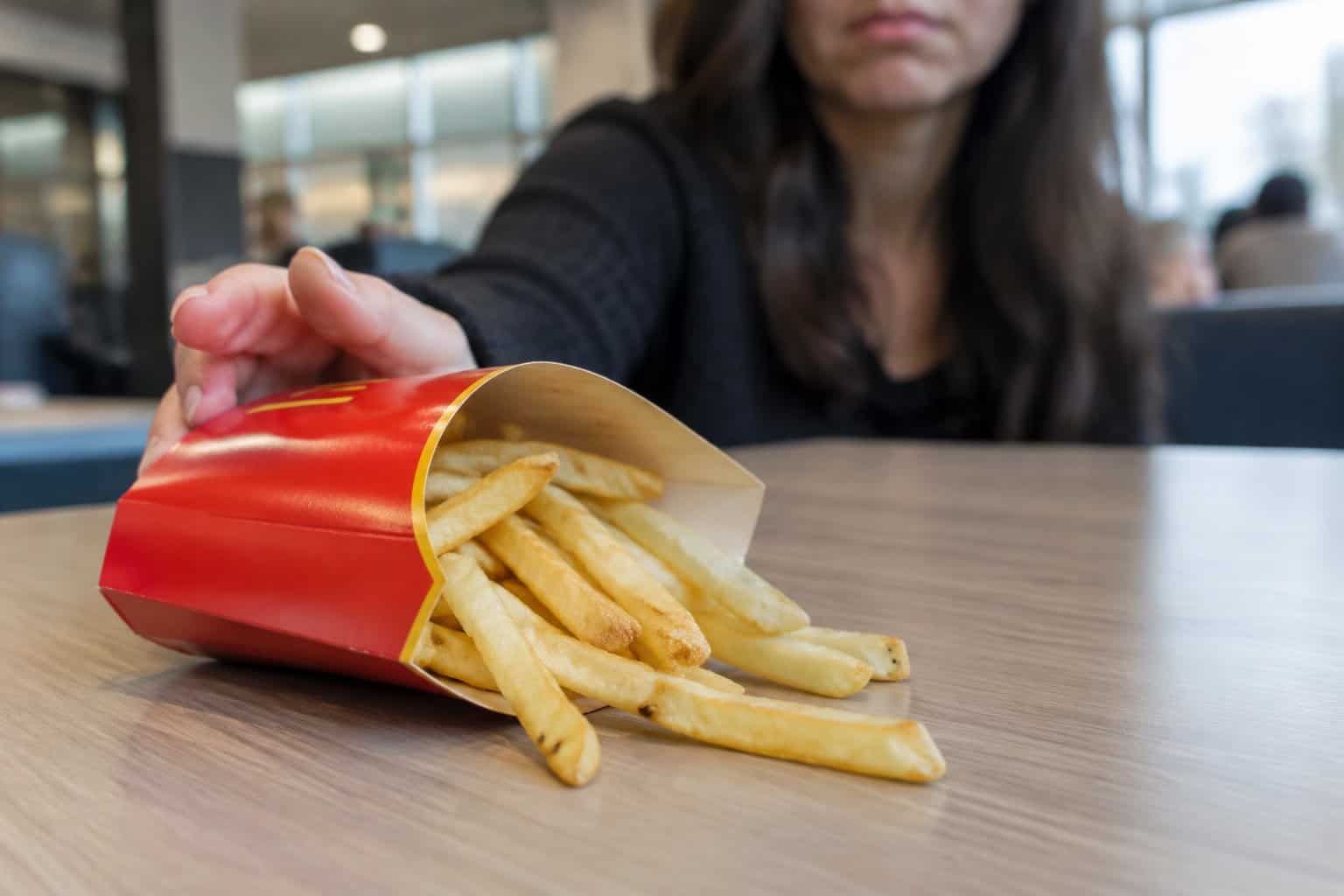 A customer pushes aside a carton of French fries on a restaurant table.