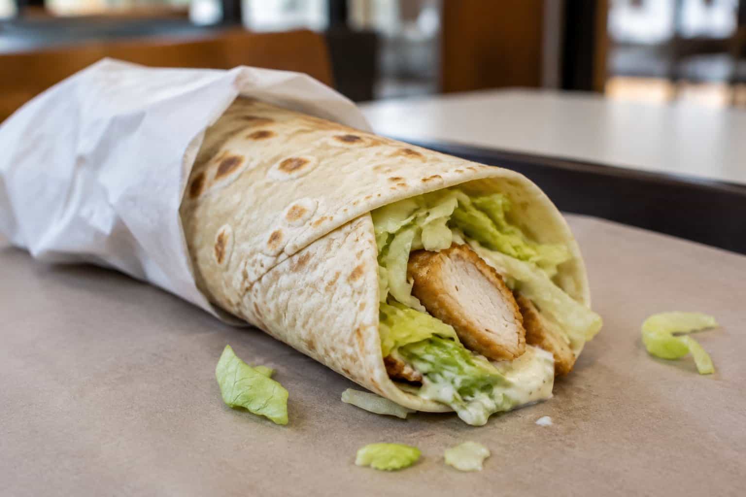 A chicken snack wrap with lettuce and sauce on a tray.