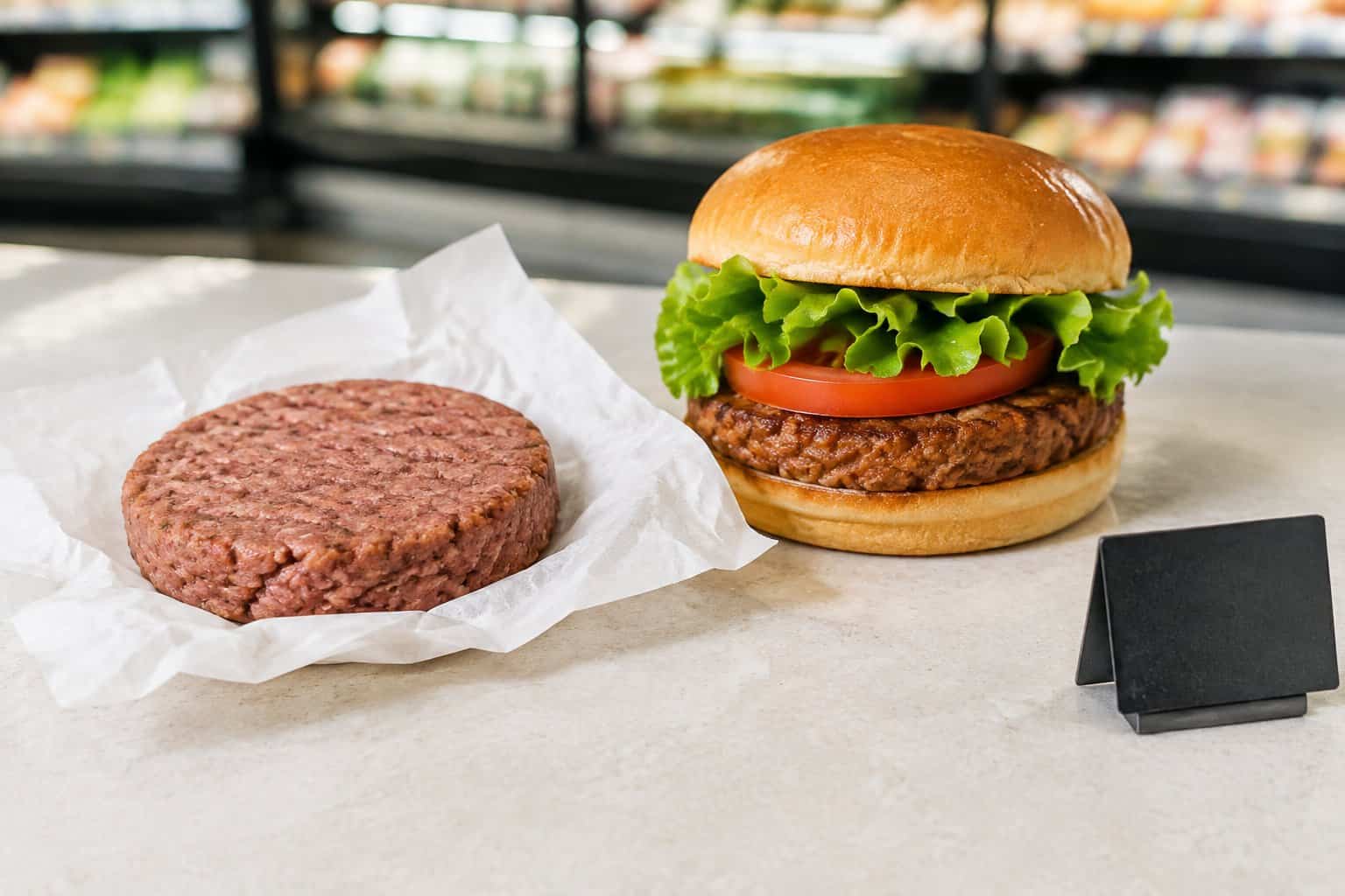 A plant-based burger patty and assembled burger beside a price tag on a grocery-store counter.