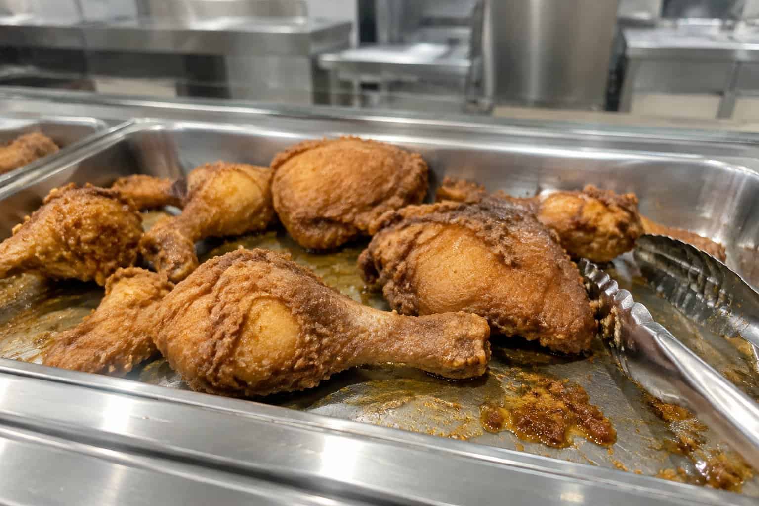 A tray of fried chicken with serving tongs at a supermarket hot bar.