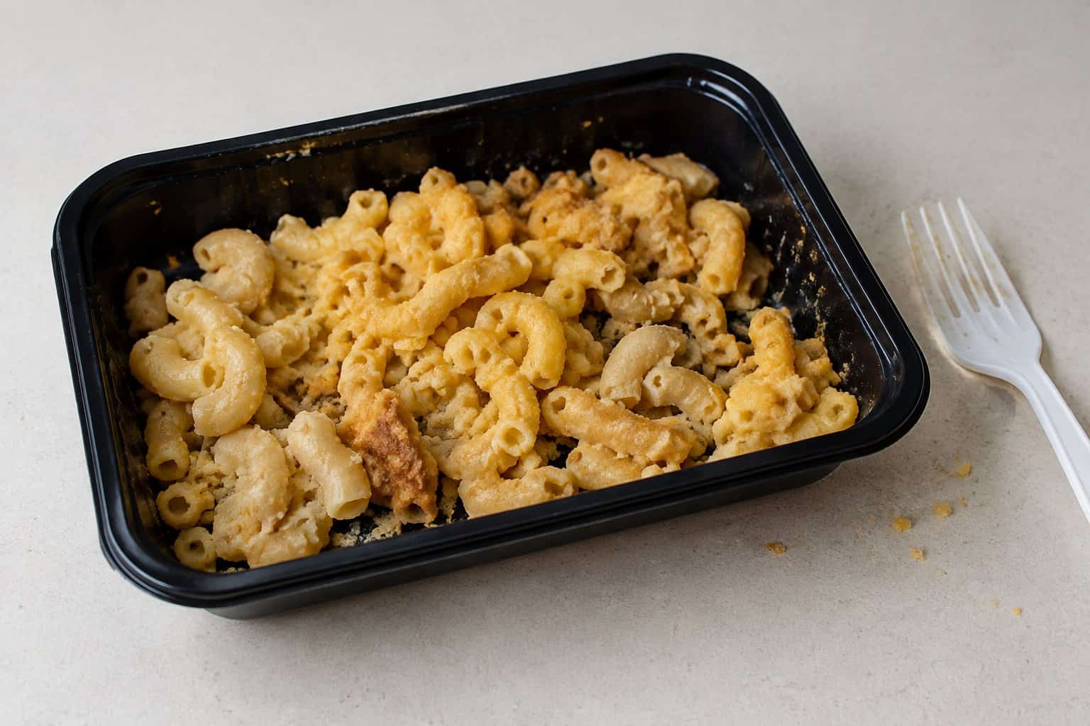 A takeout tray of dry-looking macaroni and cheese on a countertop.