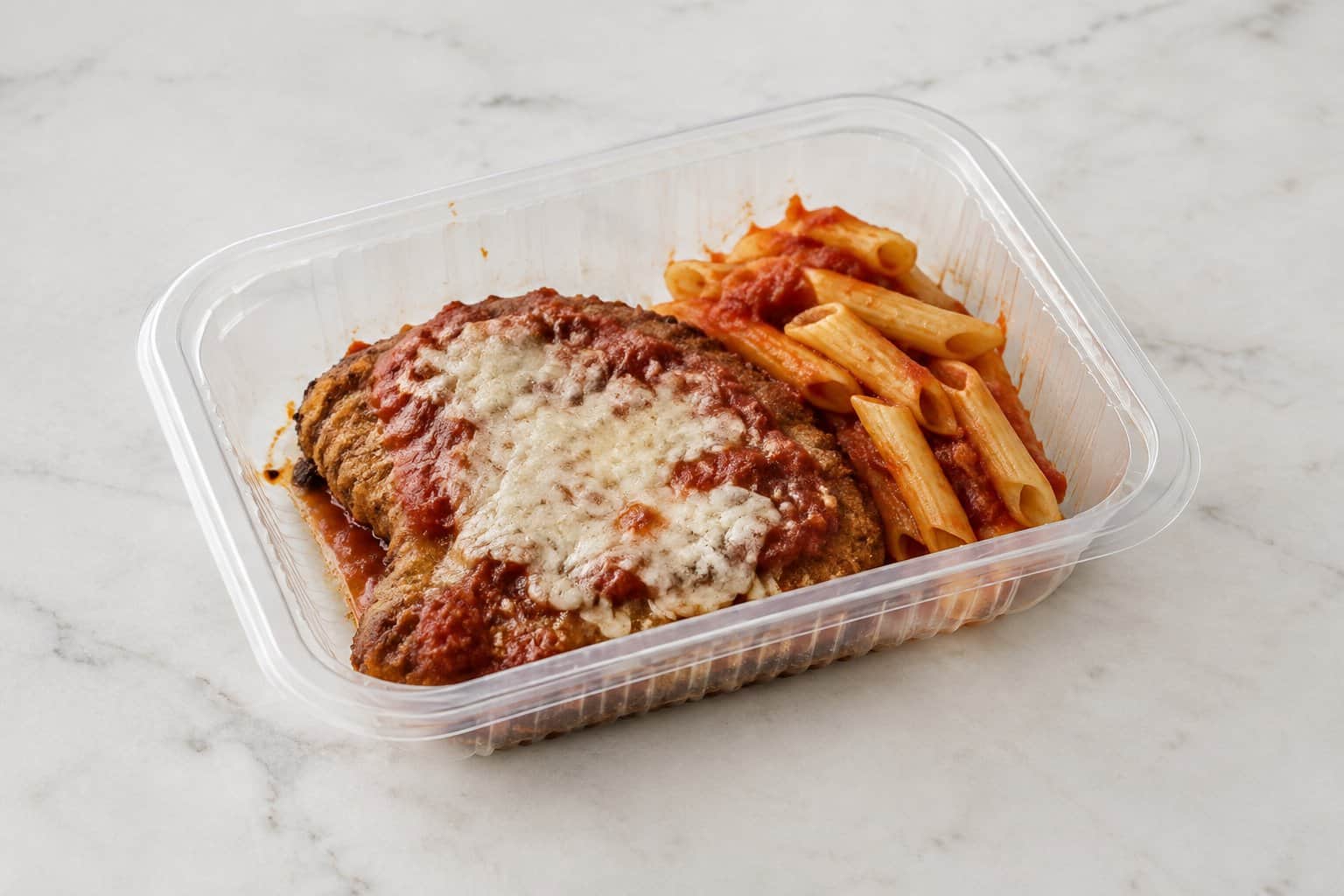 A tray of prepared chicken Parmesan with pasta on a kitchen counter.