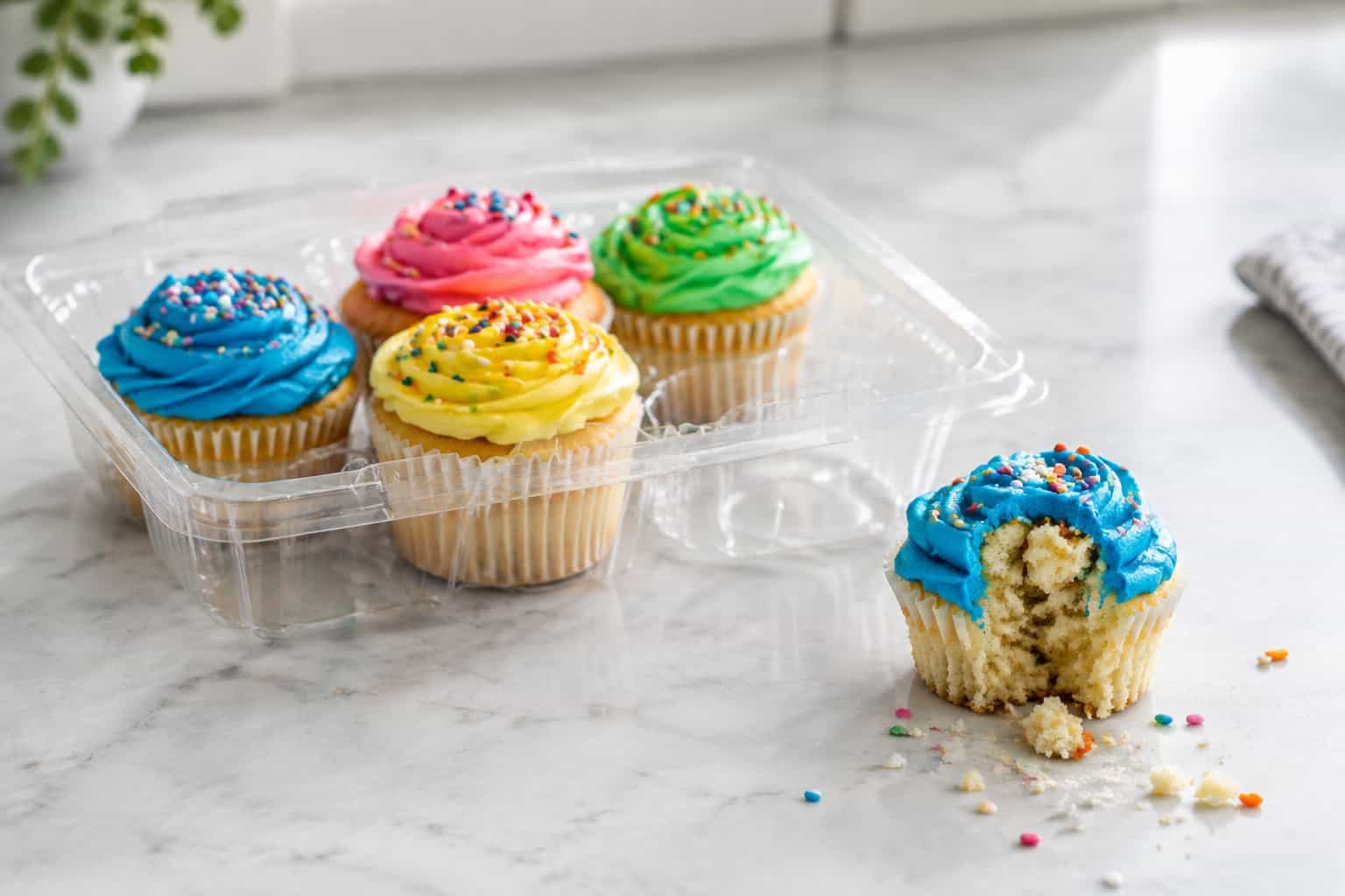 Frosted cupcakes in a clear container on a kitchen counter.