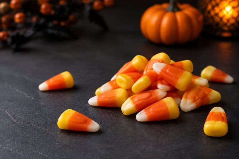 Candy corn pieces scattered on a dark surface beside a small pumpkin.