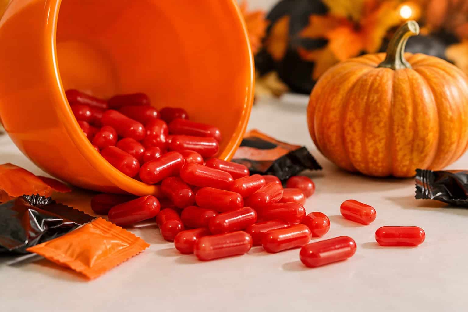 Red cinnamon candies spill beside a small pumpkin and an orange bowl.