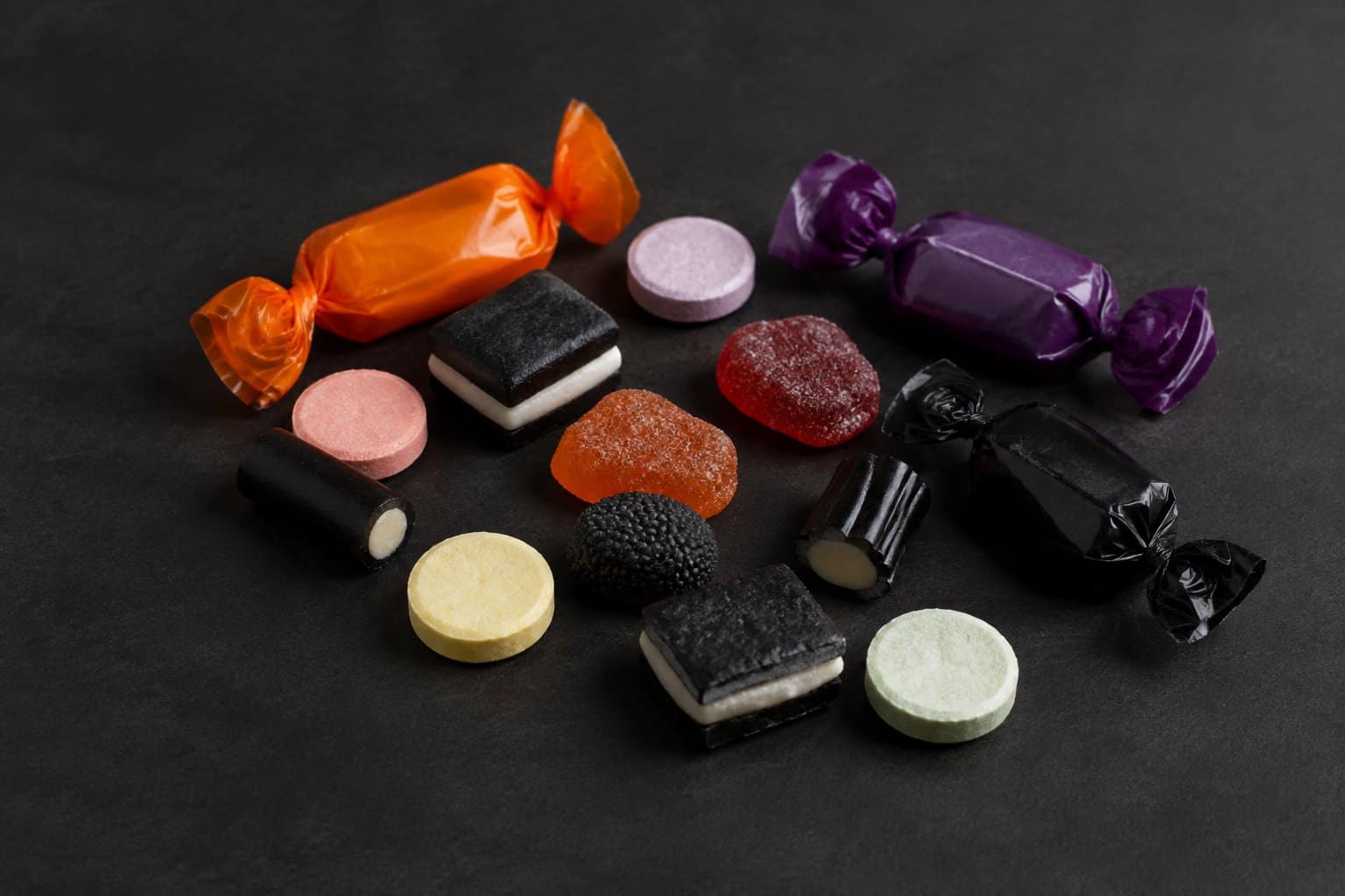 An assortment of Halloween candies scattered across a dark tabletop.
