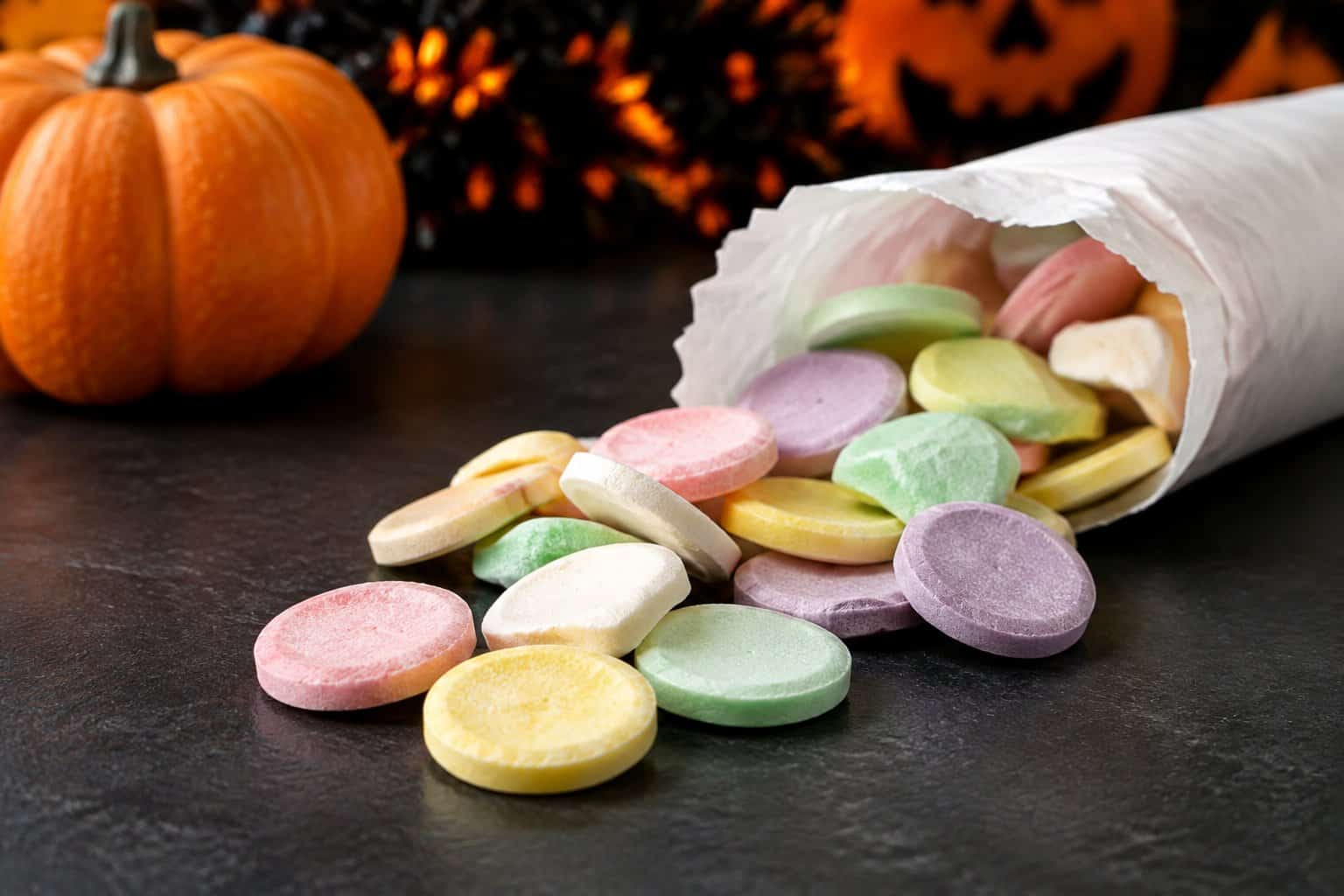Pastel candy wafers spill from an open wrapper beside a small pumpkin.