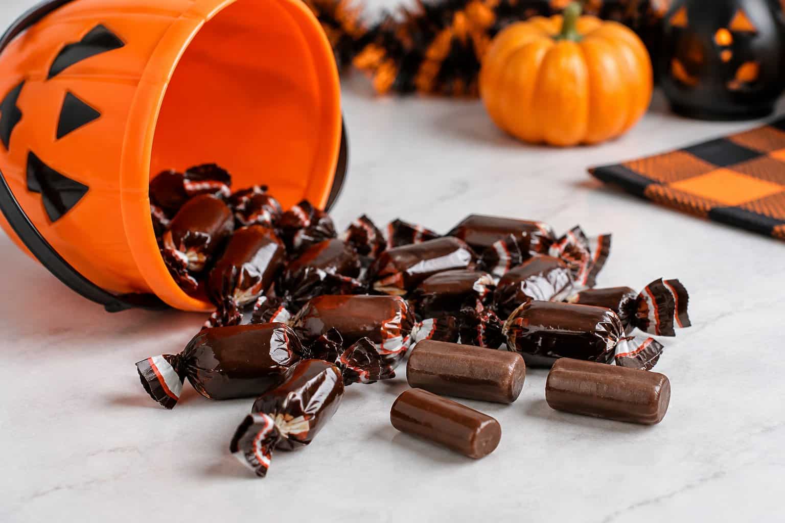 Wrapped Tootsie Rolls are scattered beside an overturned Halloween candy bowl.