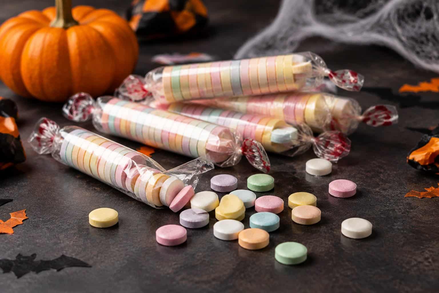 Pastel candy tablets and open candy rolls scattered on a Halloween-themed tabletop.