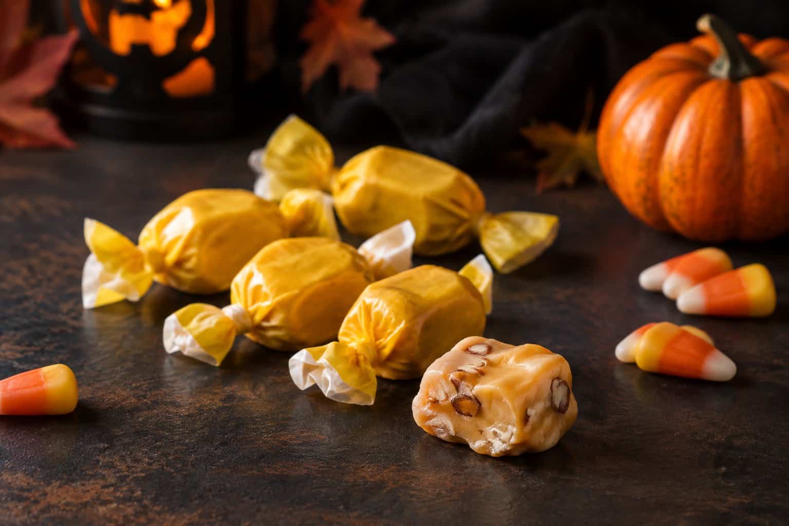 Wrapped honey taffy candies and an unwrapped piece beside candy corn and a small pumpkin.