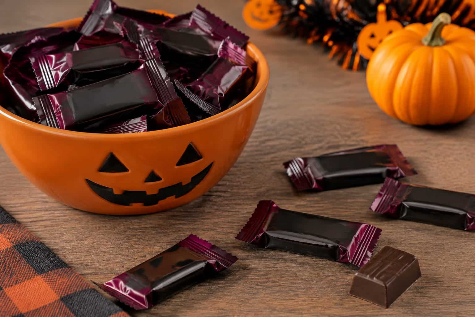 Dark chocolate candy bars scattered beside a Halloween candy bowl.