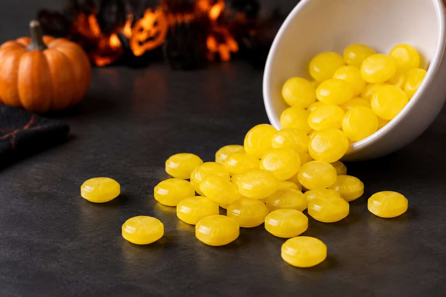 Yellow candies spill from a bowl beside a small pumpkin.