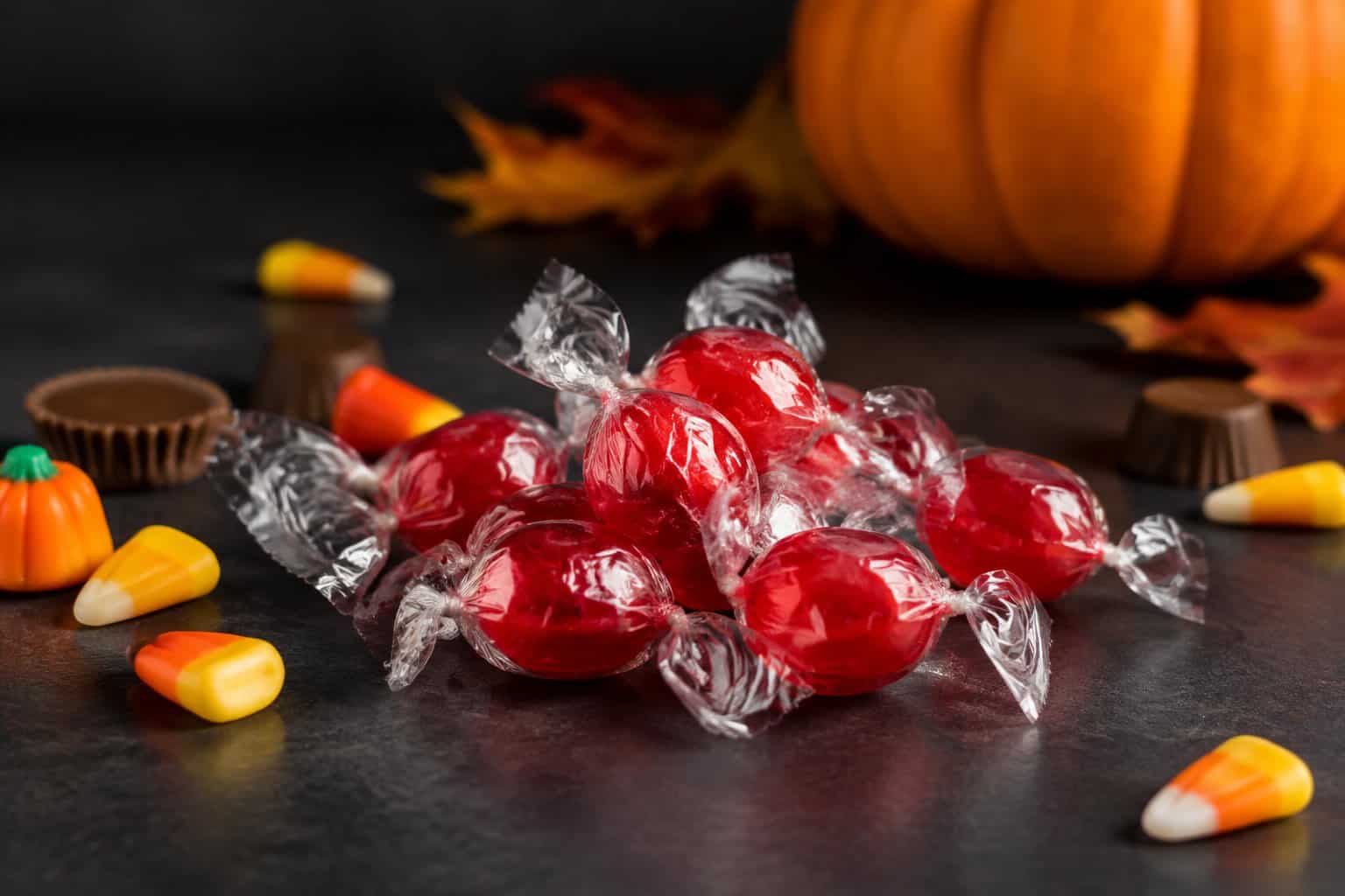 Red wrapped candies arranged with other Halloween candy near a pumpkin.