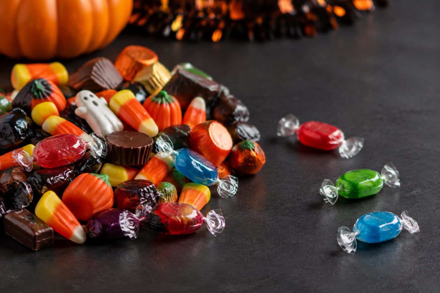 Colorful wrapped candies sit among Halloween treats beside a small pumpkin.
