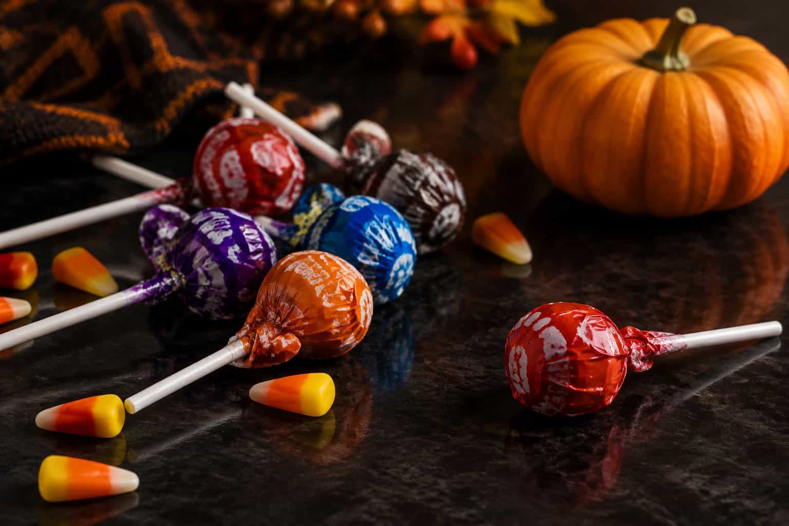 Wrapped lollipops scattered beside a small pumpkin and candy corn.