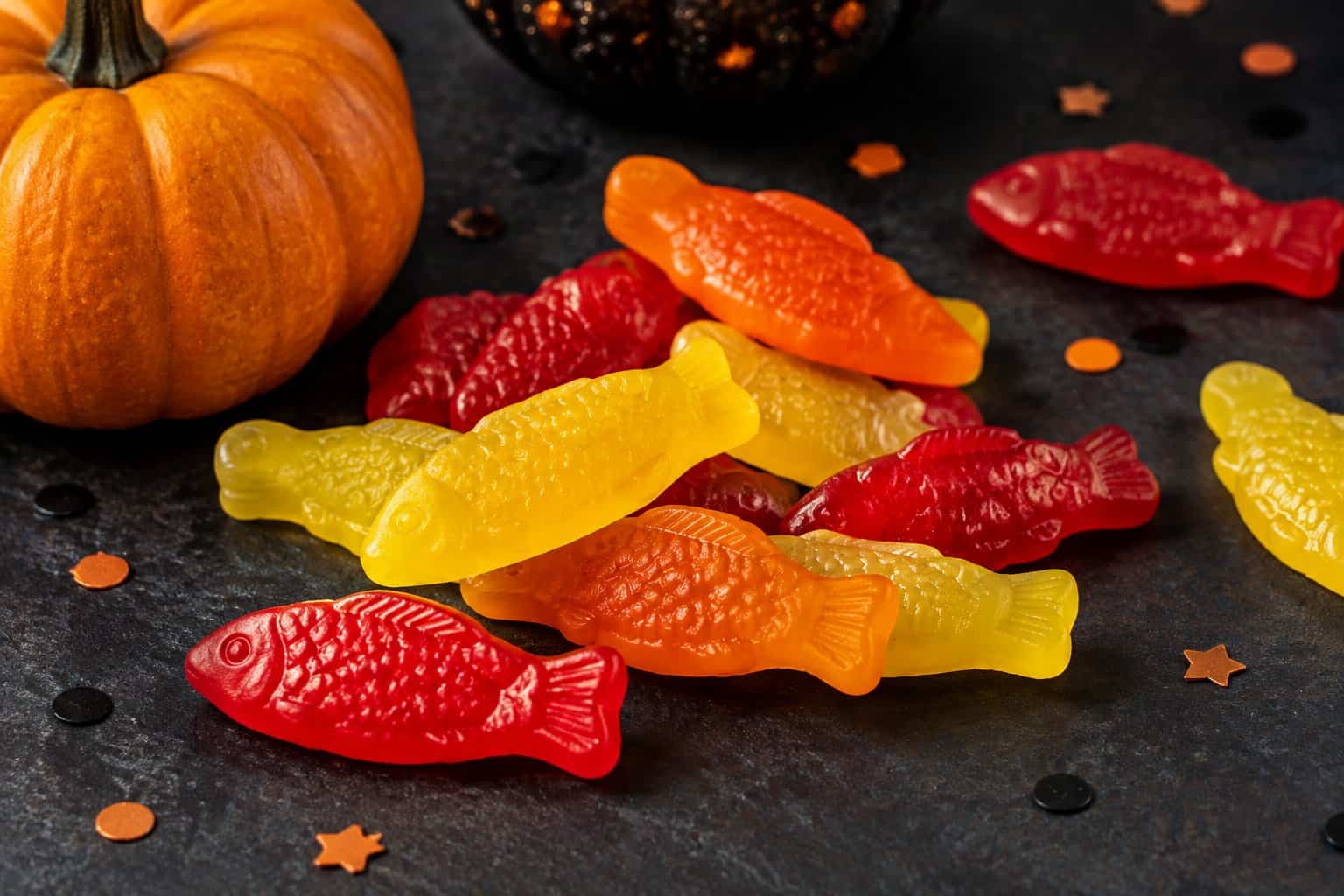 Colorful fish-shaped gummy candies arranged beside a small pumpkin.