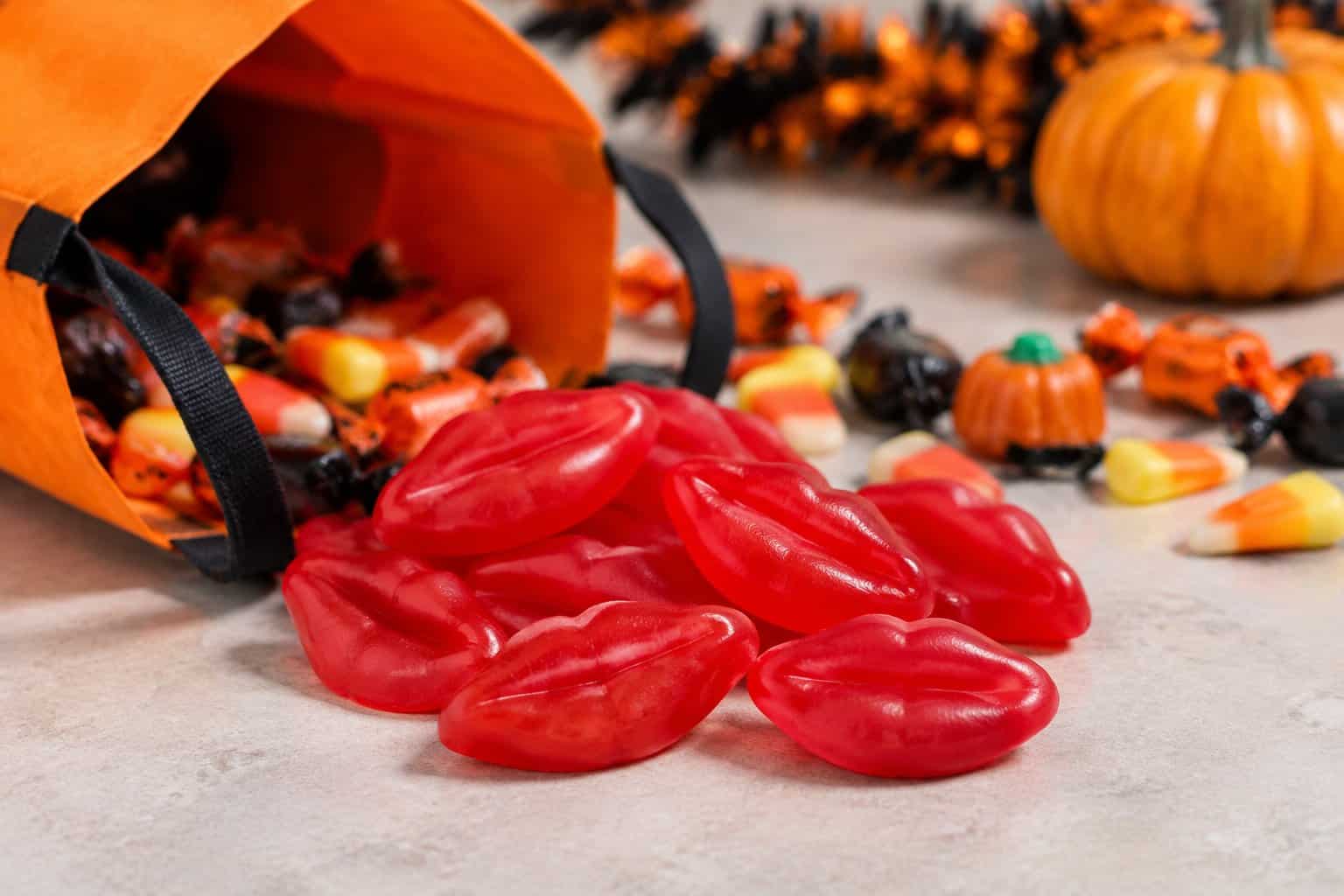 Bright red wax lips candies beside an open trick-or-treat bag.