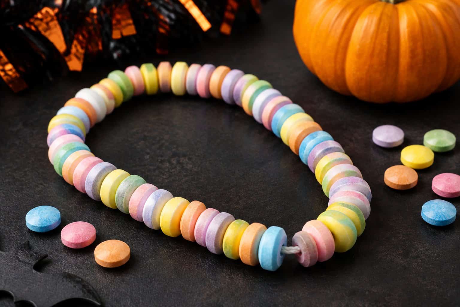 A colorful candy necklace arranged beside loose candies and a small pumpkin.