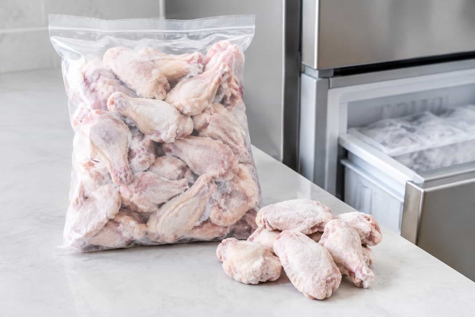 A bag of frozen chicken wings beside several raw wings.