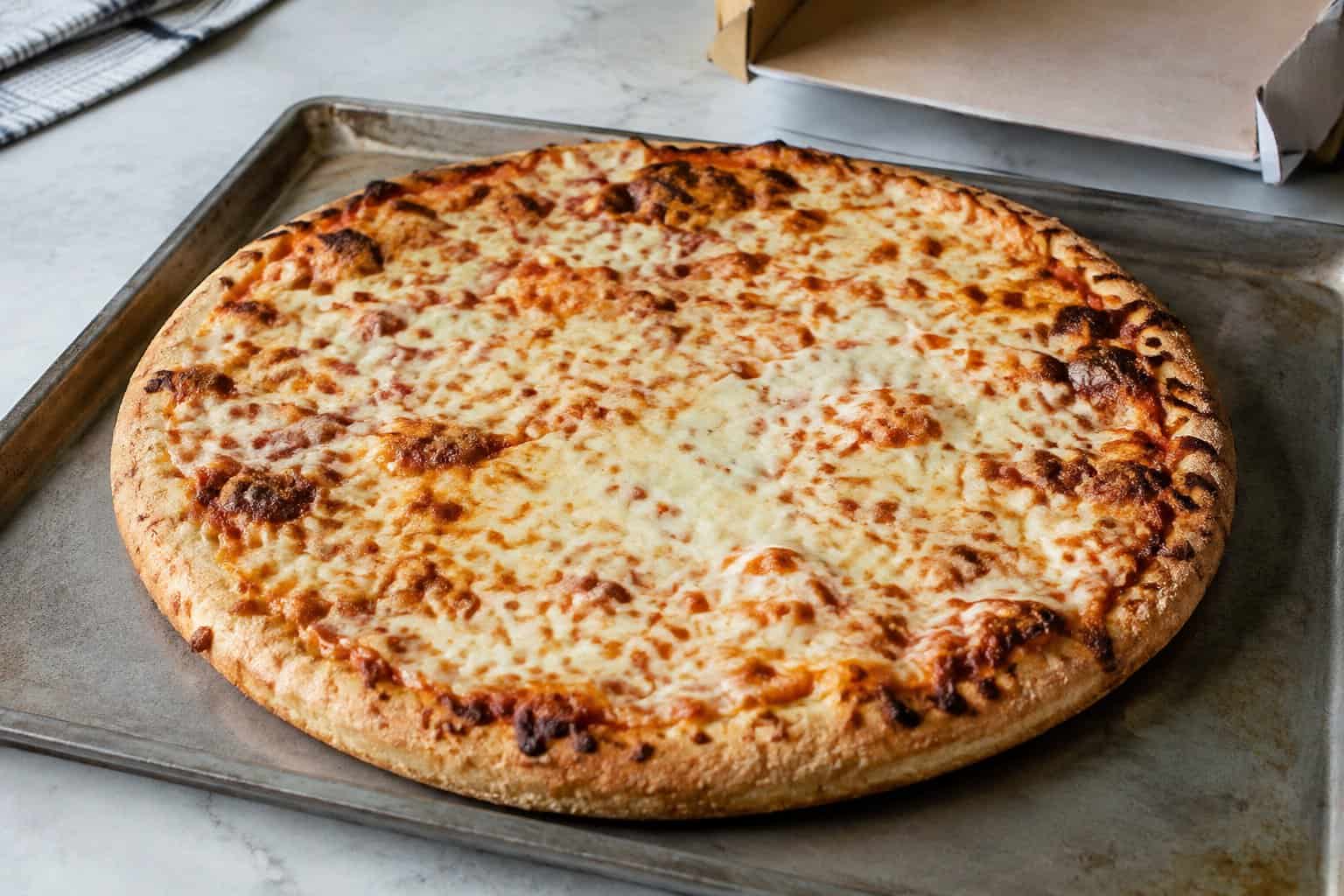 A cheese pizza with unevenly browned cheese on a baking tray.